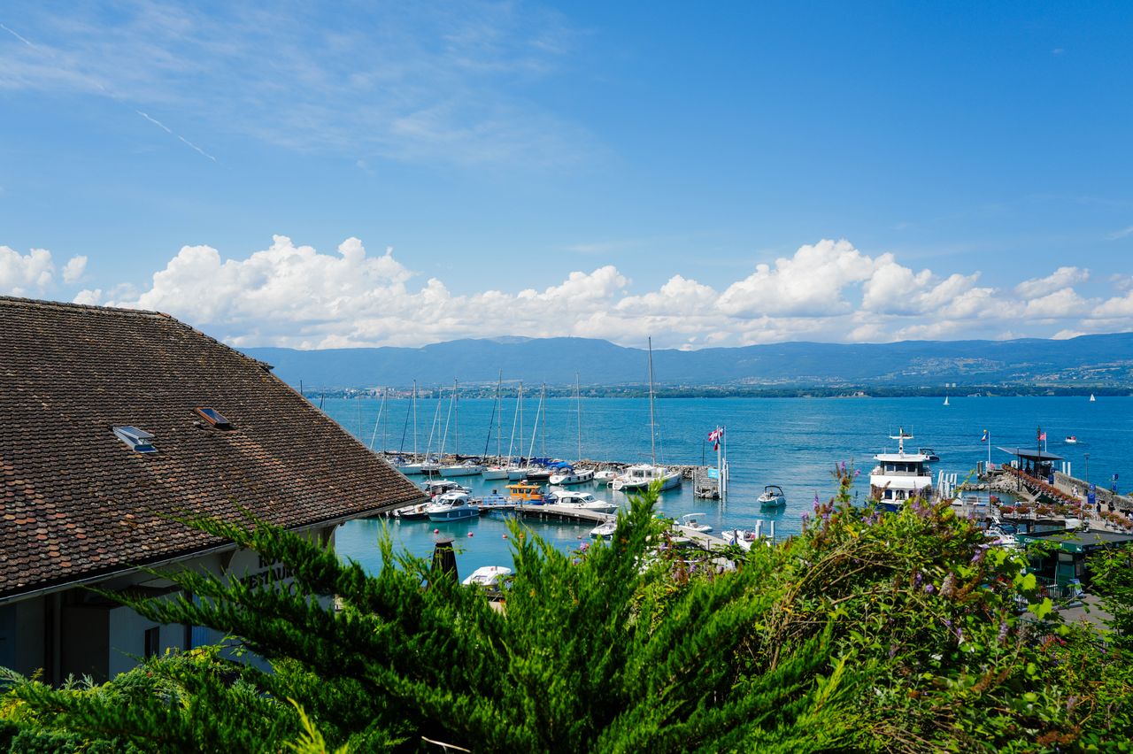 A tranquil harbor scene with boats, a house, and distant mountains under a clear sky.